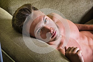 Photo of a handsome blond man with muscular physique lounging on a couch