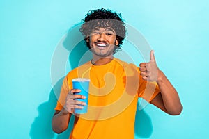 Photo of handsome guy toothy smile hold soda drink straw cup demonstrate thumb up isolated on teal color background