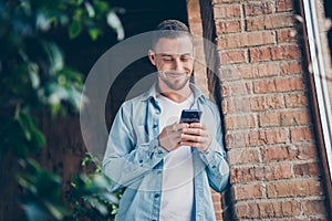 Photo of handsome homey guy leaning brick design wall near window hold telephone hands read funny jokes smiling bored