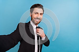 Photo of handsome positive teacher guy dressed black suit taking selfie fixing tie empty space isolated blue color