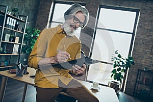 Photo of handsome senior man wear yellow shirt glasses signing contract papers indoors workshop workplace