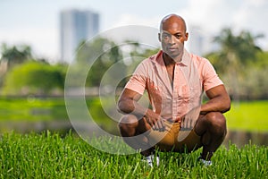 Photo handsome young African American man squatting on grass in the park. Deadpan expression staring deep into the camera photo