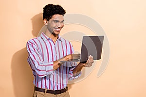 Photo of handsome young male device netbook typing message dressed stylish striped formalwear outfit isolated on beige