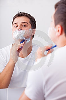 Photo of handsome young man shaving and looking at himself in th