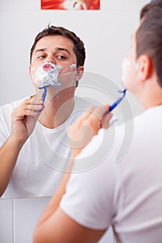 Photo of handsome young man shaving and looking at himself in th