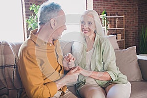 Photo of happy affectionate old couple sit sofa hold hands harmony love indoors inside house home flat