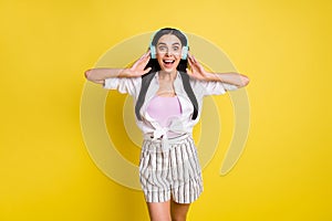 Photo of happy amazed young woman listen music headset shocked sound isolated on yellow color background
