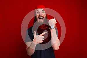 Photo of happy bearded guy, pointing at his newa watch, and dela