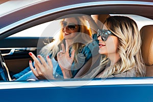 Photo of happy blondes wearing sunglasses while driving in car photo