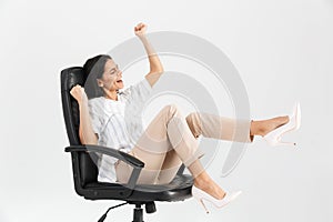 Photo of happy brunette businesswoman 30s smiling and rejoicing while sitting in black armchair in office