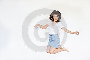 Photo of a happy brunette with pink headphones in white blouse and denim skirt jumping in the air
