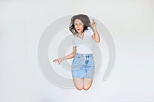 photo of a happy brunette in white blouse and denim skirt jumping in the air
