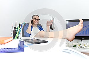 Relaxed and winning business woman sitting with her legs on desk and looking at her shoes