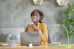 Photo of happy dreamy dark skin young business woman sit office desk relax drink coffee job indoors workstation