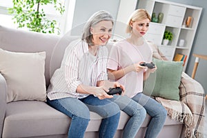 Photo of happy grandmother and upset young woman sit sofa play game joystick weekend indoors inside house