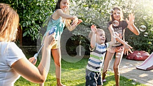 Photo of happy laughing children blowing and cathcing soap bubbles at house backyard. Family playing and having fun