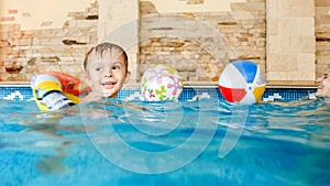 Photo of happy laughing and smiling little boy playing with toys and learning swimming in indoors swimming pool