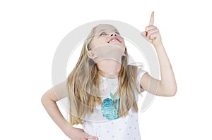 Photo of happy little girl standing isolated over white wall background. Looking up showing copyspace pointing.