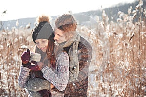 Photo of happy man and pretty woman with cups outdoor in winter. Winter holiday and vacation. Christmas couple of happy