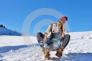 Photo of happy mother and child playing in the snow with a sledge in a sunny winter day