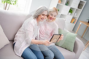 Photo of happy nice pretty old lady and young woman sit sofa look picture nostalgia family indoors inside house