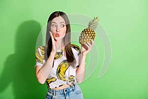 Photo of happy nice young woman hold hand pineapple cheekbone send air kiss isolated on green color background