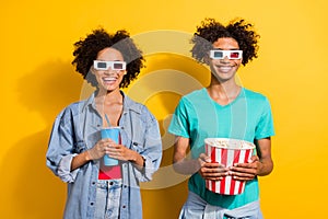 Photo of happy positive afro american couple watch movie glasses eat pop corn isolated on yellow color background