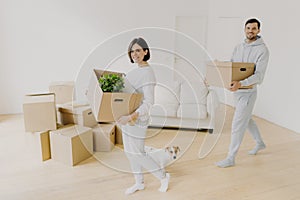 Photo of happy smiling brunette woman and her husband carry cardboard boxes with personal belongings, relocare to new apartment,