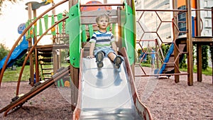 Image of happy smiling cheerful toddler boy riding and climbing on the big children playground at park