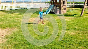 Image of happy smiling and laughing toddler boy running on green grass at children playground