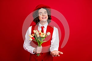 Photo of happy teenage boyfriend wearing formal suit gives you a hand invitation event and bunch tulips isolated on red