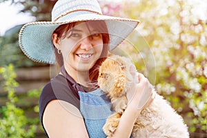 Photo of happy woman in hat holding ginger cat in garden