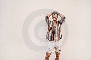 Photo of happy young hipster man, smiling, posing on the wall outdoors. Fashionable boy. Real people emotions