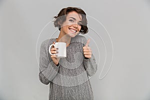 Happy young lady drinking tea showing thumbs up gesture.