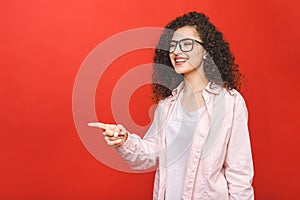 Photo of happy young student woman standing isolated over red wall background. Looking camera showing copyspace pointing