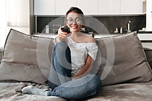 Happy young woman sitting on sofa at home watch TV.