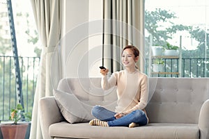 Photo of happy young woman sitting on sofa at home. Looking camera holding remote control watch TV