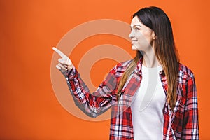 Photo of happy young woman standing isolated over orange wall background. Looking camera showing copyspace pointing
