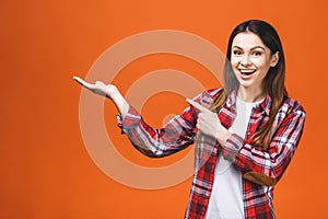 Photo of happy young woman standing isolated over orange wall background. Looking camera showing copyspace pointing