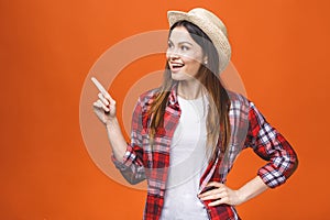 Photo of happy young woman standing isolated over orange wall background. Showing copyspace pointing