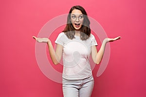 Photo of happy young woman standing isolated over pink background. Looking camera showing copyspace pointing.