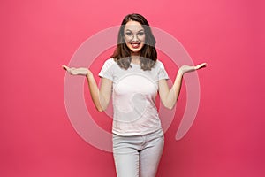 Photo of happy young woman standing isolated over pink background. Looking camera showing copyspace pointing.