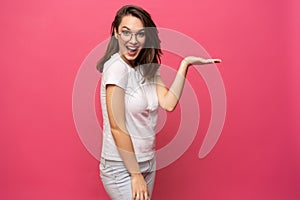 Photo of happy young woman standing isolated over pink background. Looking camera showing copyspace pointing.