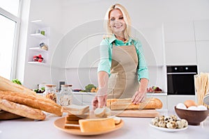 Photo of housewife lady slice baguet bread hold slice put dish prepare lunch wear apron kitchen room indoors