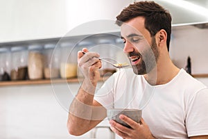 Photo of hungry young man eating breakfast from bowl.