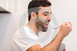 Photo of hungry young man eating breakfast from bowl.