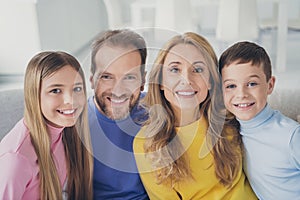 Photo of idyllic family mom dad and two children boy girl look in camera toothy smile sit couch in house indoors