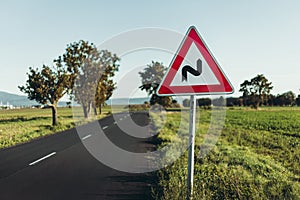 Photo of illuminated and warning road sign - double curve next to the road on meadow. Double Bend warning road sign on country