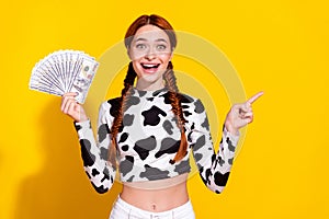 Photo of impressed excited lady dressed cowskin print top holding cash fan pointing empty space isolated yellow color photo