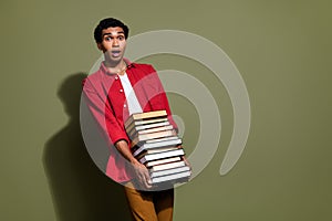 Photo of impressed funny man dressed red shirt carrying huge book pile empty space isolated green color background